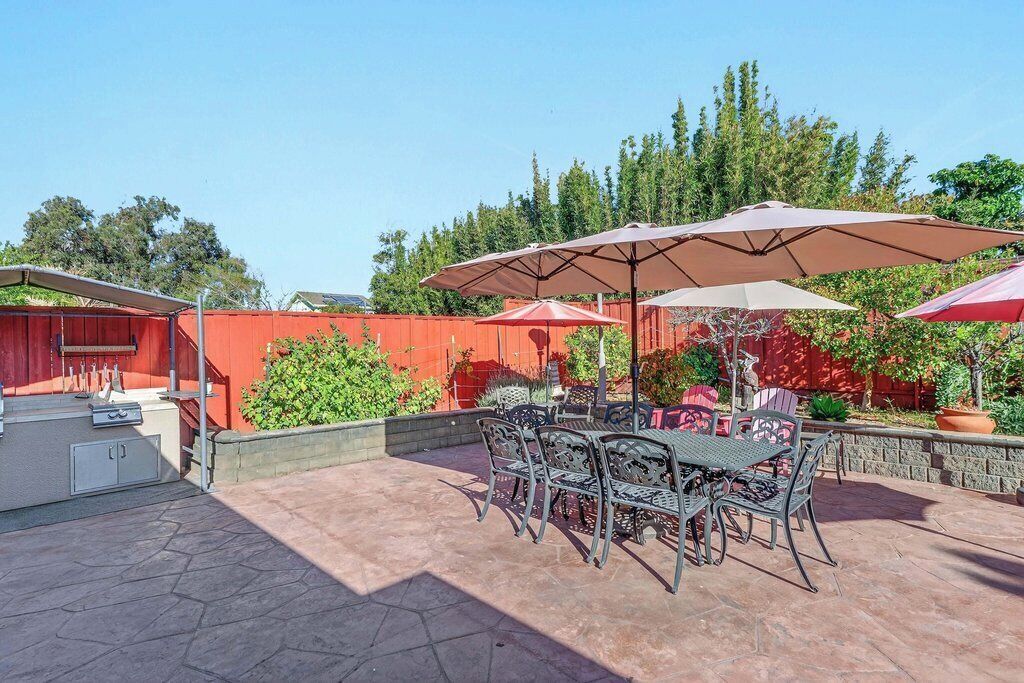 An outdoor patio with a barbecue grill, metal chairs, and umbrellas.