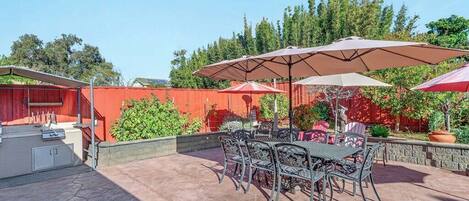 An outdoor patio with a barbecue grill, metal chairs, and umbrellas.