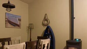 A cozy room with a wooden dining table and chairs, a wall-mounted lamp, a decorative item, and a wood-burning stove. - A perfect weekend gateway! (Grafton)