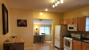 A kitchen with wooden cabinets, a refrigerator, a microwave, an oven, and a dining area with a table and chairs. - A perfect weekend gateway! (Grafton)