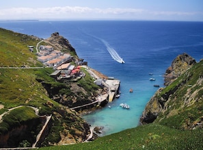 A coastal village with houses along the cliffside, a small pier, and boats in the water.