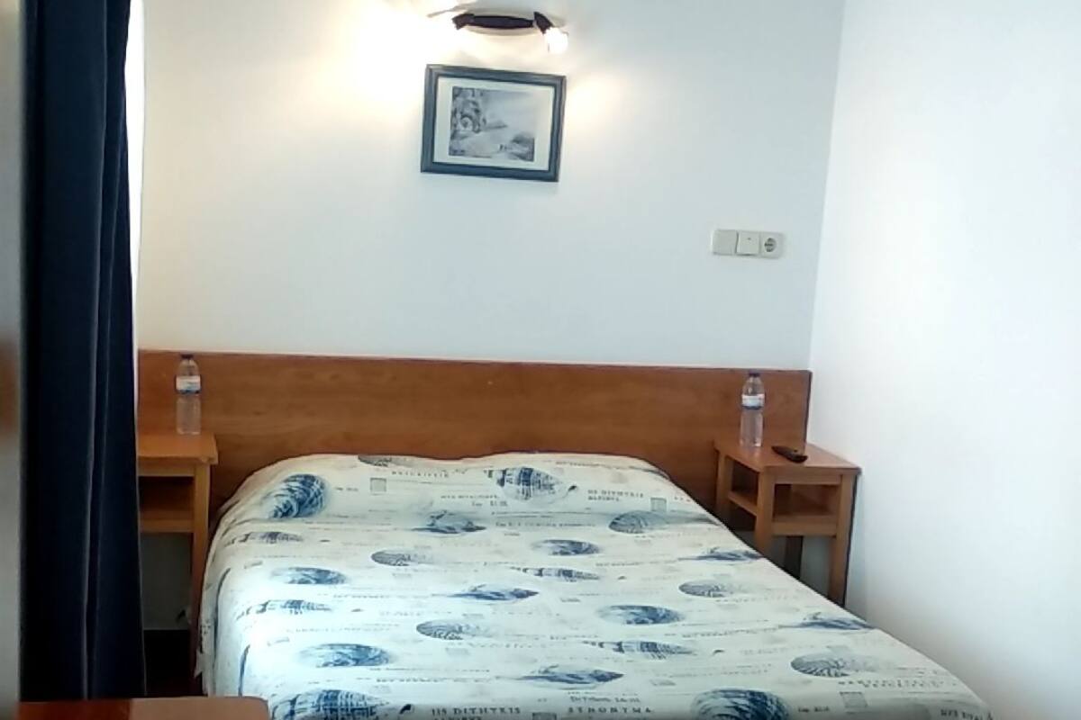 A bedroom with a bed, a nightstand, a table, and a wall-mounted light fixture.
