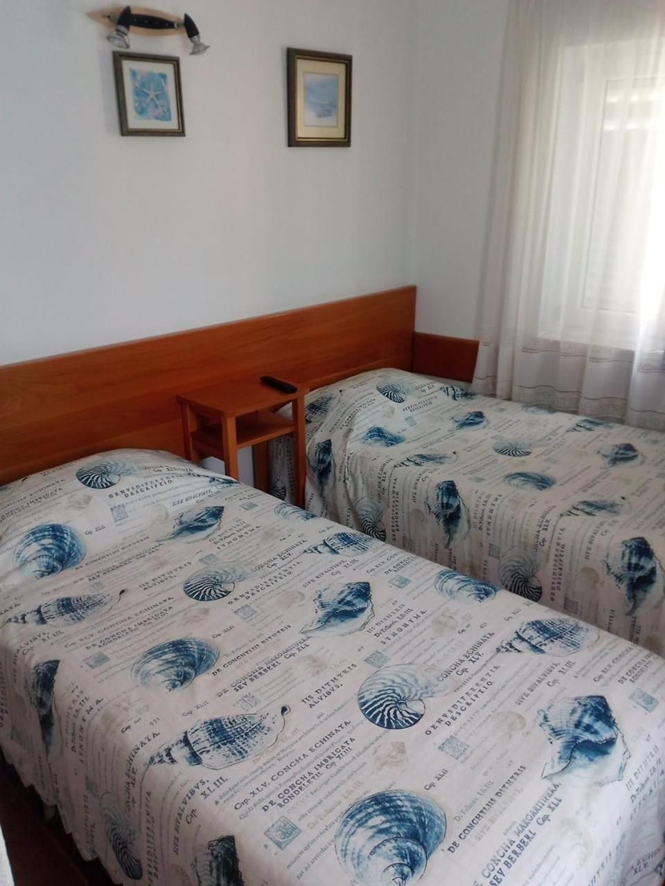 A hotel room with two beds, a wooden headboard, a small table, and two framed pictures on the wall.