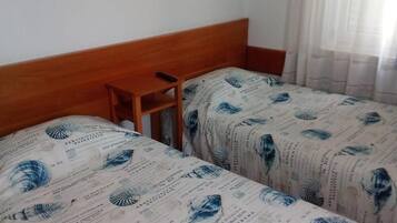 A hotel room with two beds, a wooden headboard, a small table, and two framed pictures on the wall.
