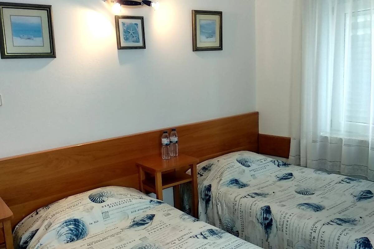 A room with two beds, a wooden headboard, a nightstand with two bottles, and three framed pictures on the wall.