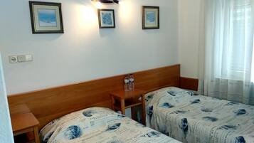 A room with two beds, a wooden headboard, a nightstand with two bottles, and three framed pictures on the wall.