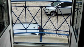 Vista desde una ventana que da a un patio interior con un edificio al fondo, una zona pavimentada y un coche estacionado.