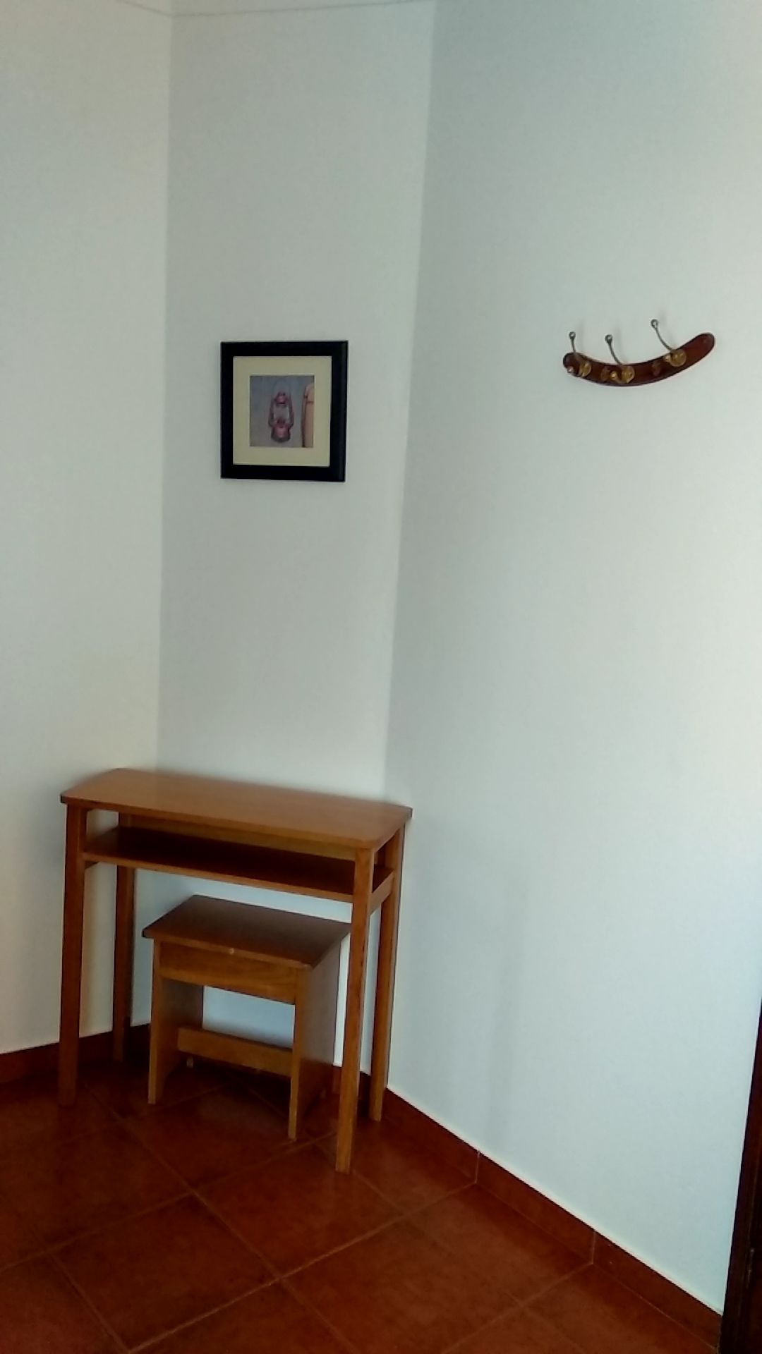Une pièce avec un bureau en bois et un petit tabouret, un tableau encadré accroché au mur et un porte-manteau avec des crochets.