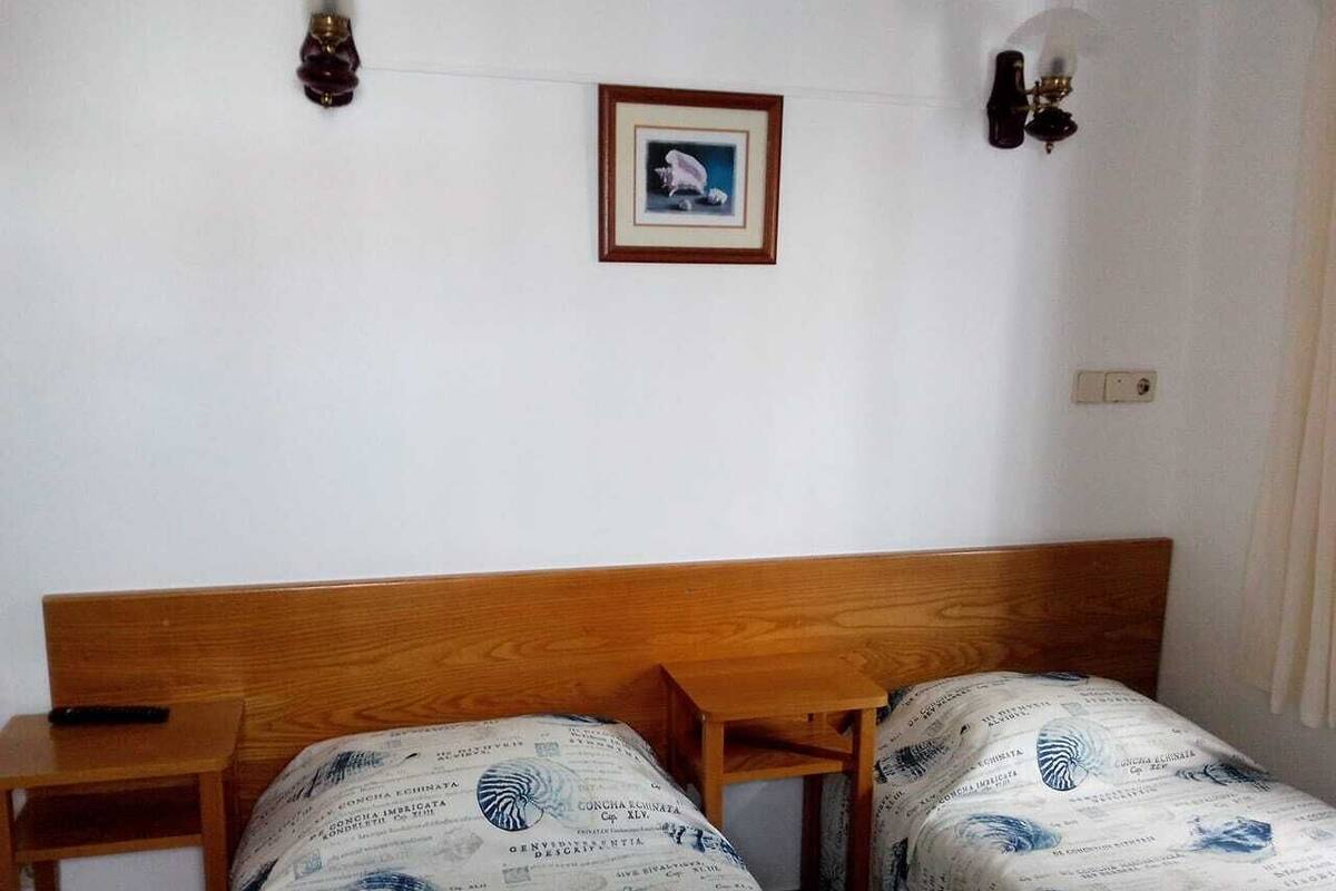 A room with two single beds, wooden headboards, a small bedside table with a lamp, and a framed picture on the wall.