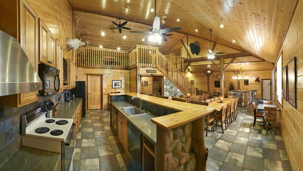 A spacious kitchen with a large island, wooden cabinetry, and a stone accent wall. - Gather Your Group at the Bunkhouse! (Port Washington)