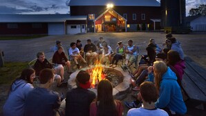 A group of people sitting around a fire pit in an outdoor setting with a building in the background. - Gather Your Group at the Bunkhouse! (Port Washington)