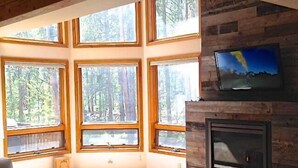 Ein Zimmer mit großen Fenstern, einem Kamin und einem an der Wand befestigten Fernseher.