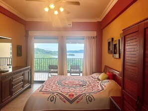 A bedroom with a large bed, a dresser, a mirror, and a balcony with a view of the water. - Million Dollar View in Heart of Flamingo w/Costa Rican Decor! (Guanacaste)