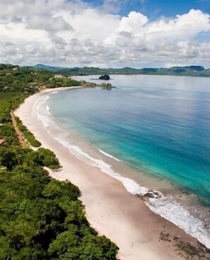 A coastal beach with a curved shoreline, dense greenery, and a clear sky. - Million Dollar View in Heart of Flamingo w/Costa Rican Decor! (Guanacaste)