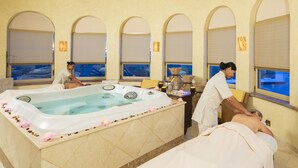 Een wellnessruimte met een ruime jacuzzi, twee massagetafels en een decoratieve vaas.