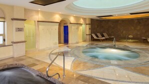 Een wellnessruimte met een jacuzzi, lounge stoelen en een zwembad.