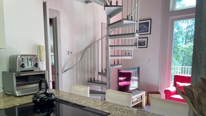Una cucina con piano cottura integrato, un tostapane e un forno a microonde. Una scala conduce a un balcone con una sedia rossa.