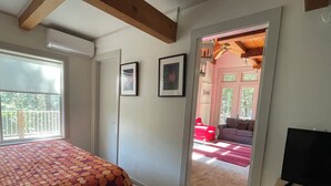 Camera da letto con un letto, una TV e una porta che dà su una zona giorno con una poltrona rossa e un divano.