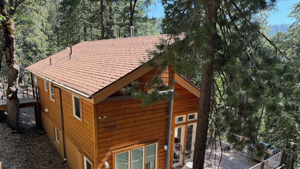 Una baita di legno con tetto rosso, ampie finestre e un patio.