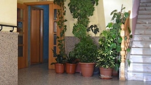 Un pasillo con puerta de madera, plantas en macetas y una escalera de mármol.