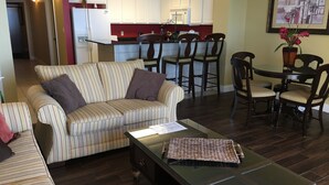 Una sala de estar con un sofá a rayas, una mesa de centro y un comedor con sillas de madera y una pequeña mesa.