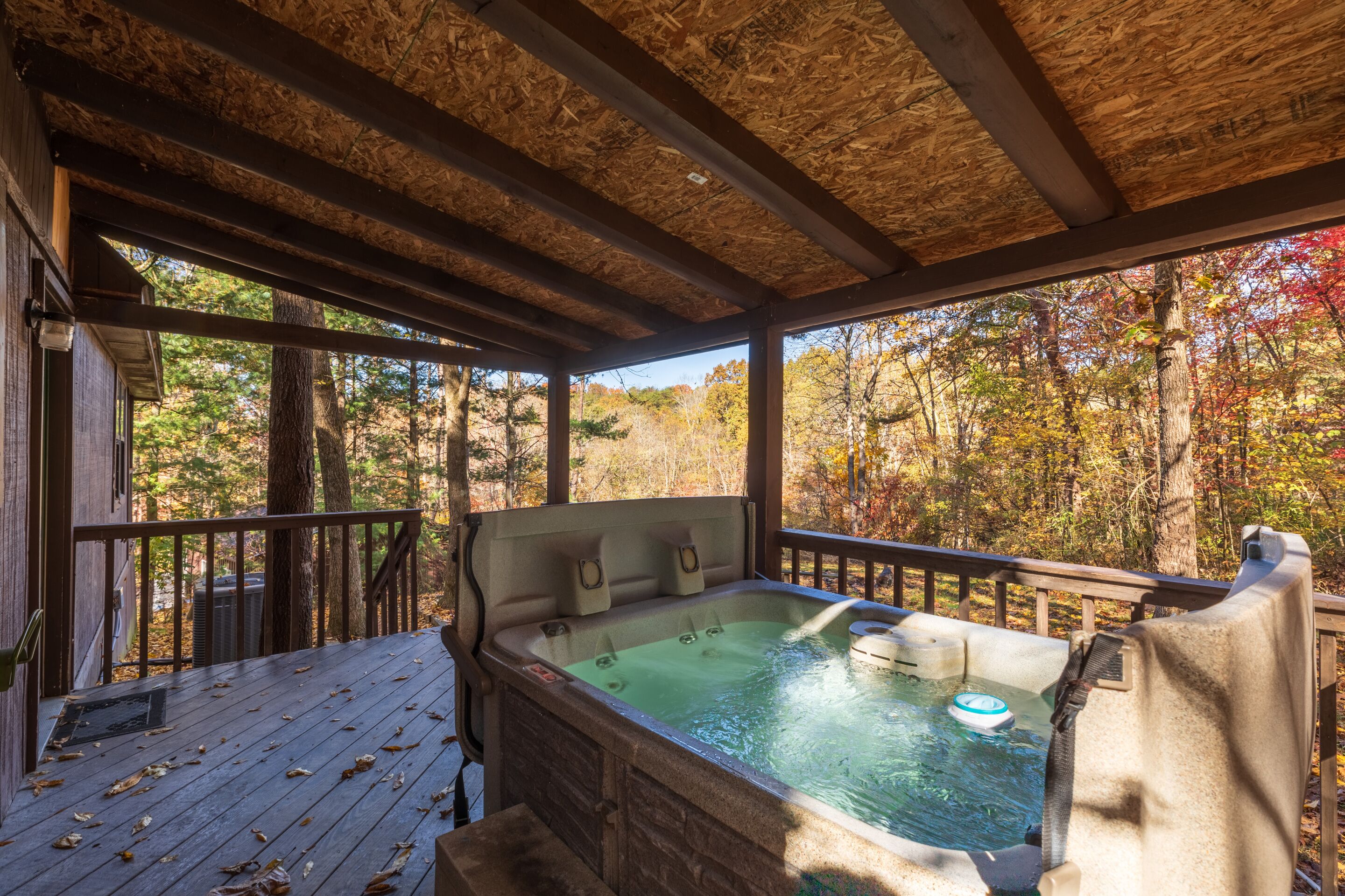 A hot tub on a wooden deck with a view of autumn trees.