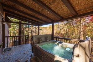 Una terraza de madera con un jacuzzi, rodeada de árboles con follaje otoñal.