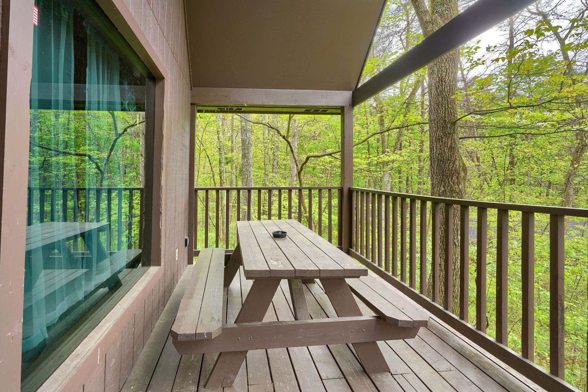 A wooden deck with a picnic table and a glass door leading to a forested area.