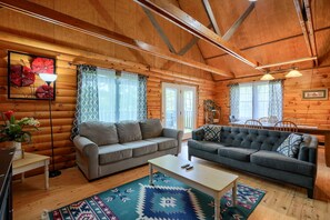 Ein gemütliches Blockhaus-Interieur mit zwei Sofas, einem Couchtisch und einem Essbereich.