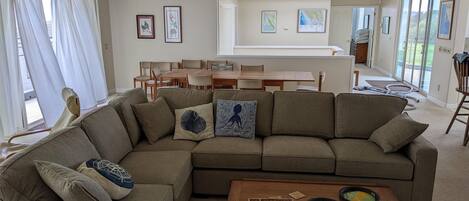 A modern living room with a sectional sofa, a wooden coffee table, and a dining area with a table and chairs.