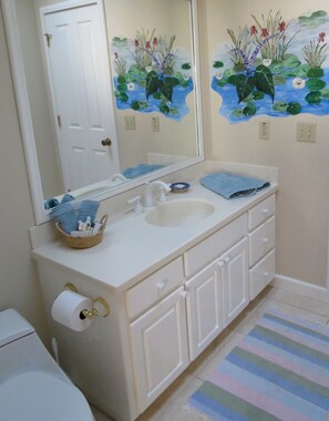 A bathroom with a white vanity, a large mirror, a toilet, and a striped rug.