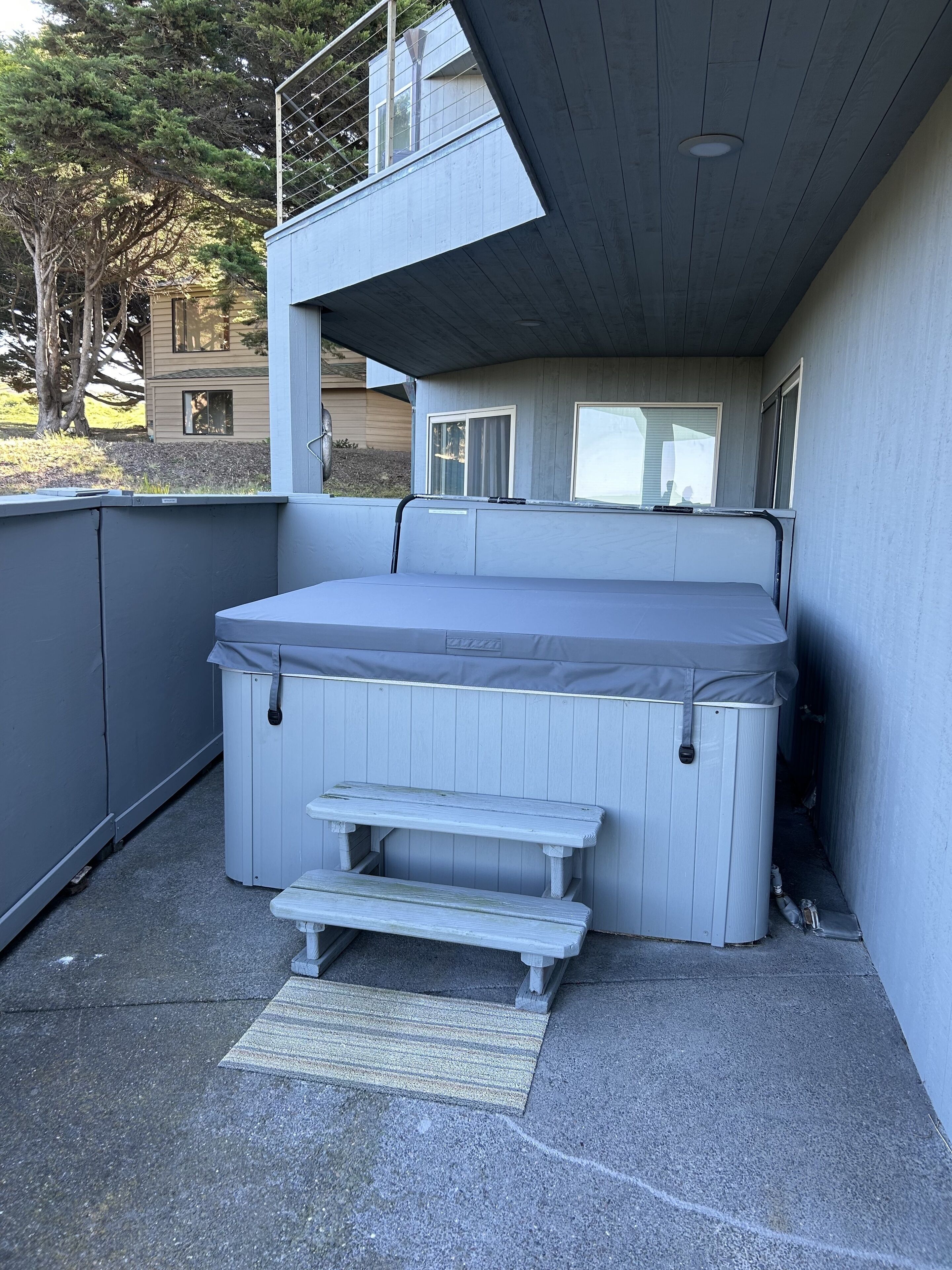 A hot tub with steps, a covered patio area, and a view of a house in the background.