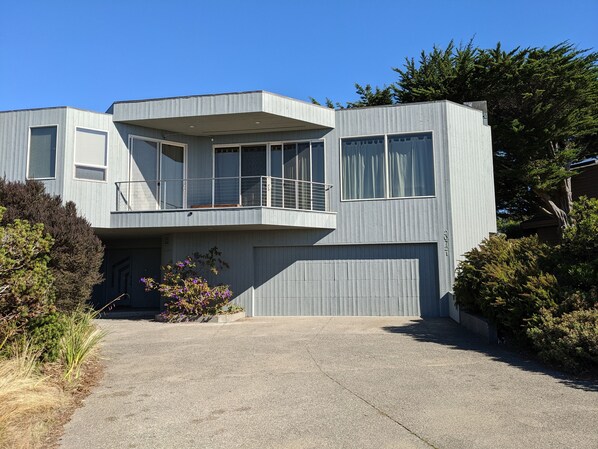 A modern two-story house with a balcony, large windows, and a garage.