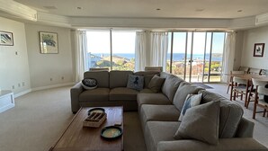A spacious living room with a large sectional sofa, a wooden coffee table, and a view of the ocean through large windows. - Spacious 5-bedrm home:Ocean Views,hot tub,BBQ,pool & ping pong tables, fast wifi (Bodega Bay)