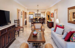 A spacious living room with a television, a dining area with chairs, a sofa, and a chandelier.