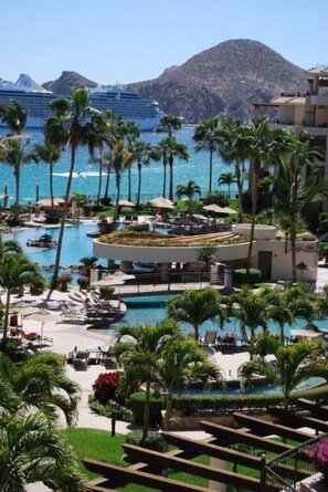 A resort with multiple swimming pools, palm trees, and a view of the ocean and cruise ships in the background. - Everything you need! Ocean views from your balcony! (Cabo San Lucas)