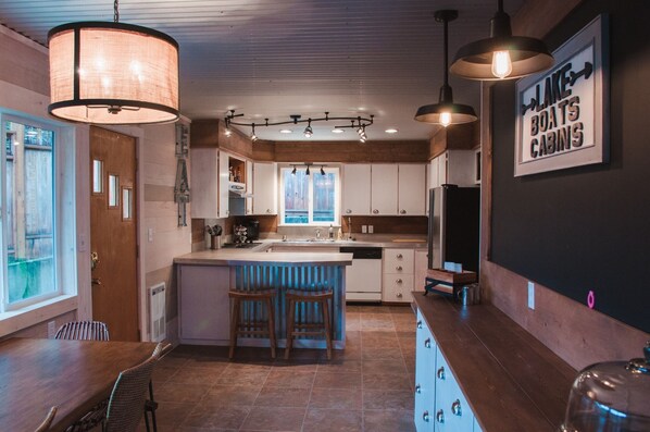 A modern kitchen with a central island, pendant lighting, and a sign reading "Lake Boats Cabins". - Fun, Relaxing, Family Friendly on Sunnypoint! (Port Angeles)