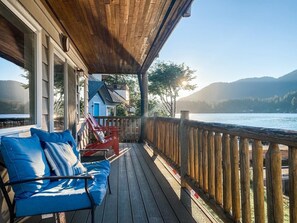 A wooden deck with a blue sofa and red chairs, overlooking a lake with mountains in the background. - Fun, Relaxing, Family Friendly on Sunnypoint! (Port Angeles)