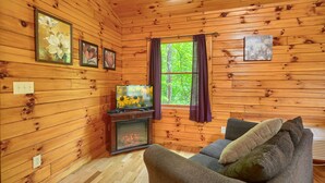 A cozy cabin interior with wooden walls, a fireplace, a sofa, and framed artwork.