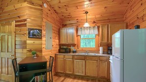 A wooden cabin interior with a kitchen area, a dining table with chairs, and a refrigerator.