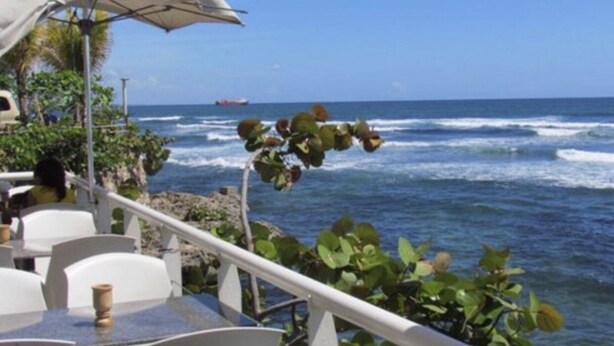 Un espace extérieur aménagé avec des tables et des chaises, offrant une vue sur l’océan et les vagues qui se brisent sur le rivage.