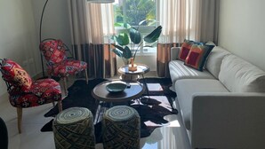 Un salon moderne avec un canapé blanc, des fauteuils à motifs, une table basse et une grande fenêtre avec des rideaux.