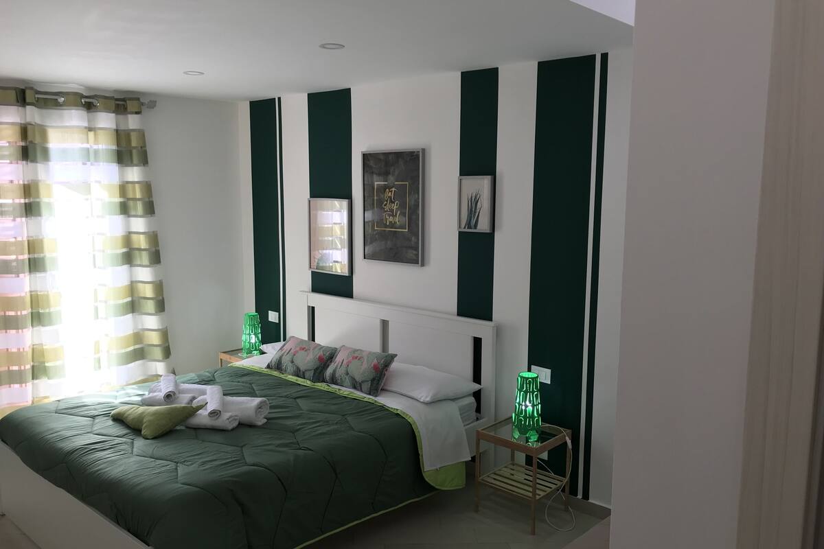 A neatly arranged bedroom with a bed, pillows, a bedside table, and a wall-mounted mirror.