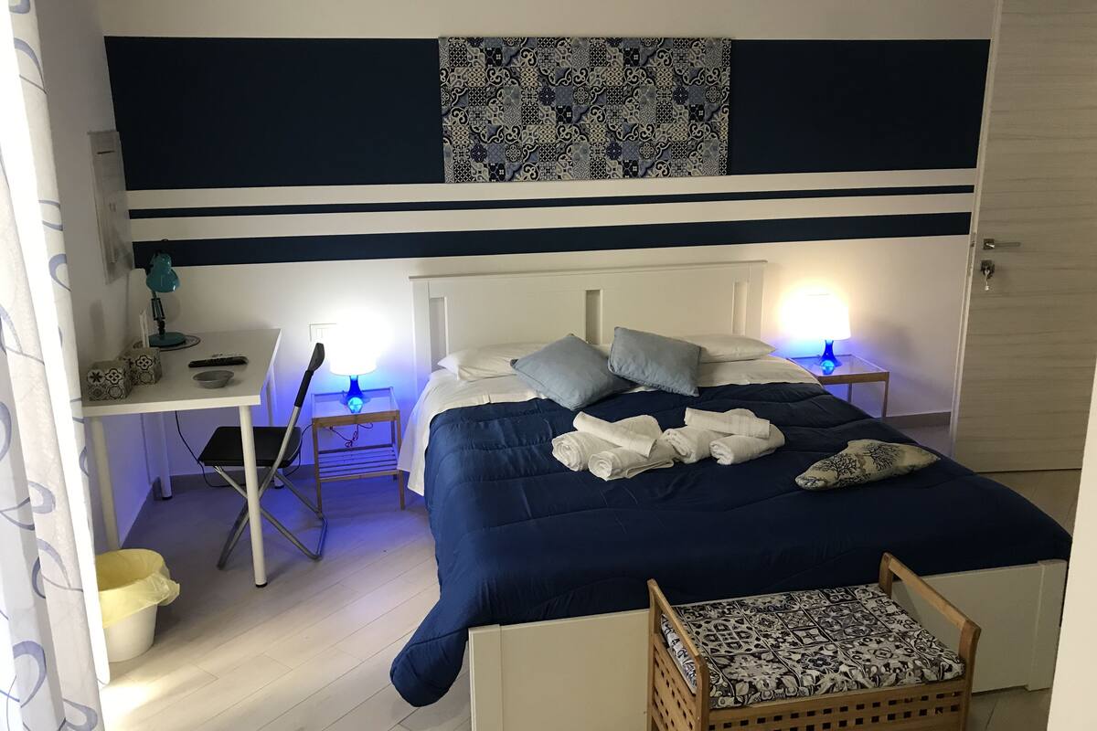 A neatly arranged bedroom with a bed, bedside tables, a desk, and a chair.