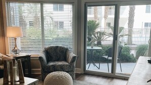 A living room with a sofa, ottoman, and a coffee table. There is a sliding glass door leading to an outdoor patio with a table and chairs. - Prime October Dates Are Open! Perfect Time For a Beach Trip! (Orange Beach)