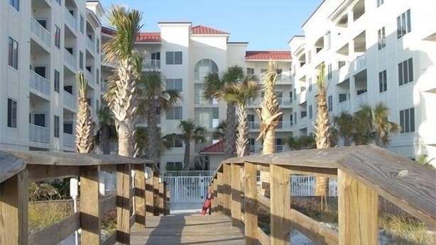 A wooden boardwalk leading to a beachfront hotel with multiple balconies and palm trees. - Prime October Dates Are Open! Perfect Time For a Beach Trip! (Orange Beach)