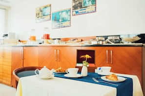 A breakfast setup with a table, a teapot, cups, a croissant, and a vase with a flower. - Arcangelo Roof Hotel (Rimini)