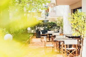 An outdoor seating area with tables and chairs, surrounded by greenery and a building in the background. - Arcangelo Roof Hotel (Rimini)