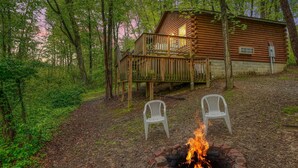 A cabin with a wooden deck, two white plastic chairs, and a fire pit. - Blue Rose Cabins - Pine Ridge Cabin (Logan)