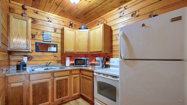 A kitchen with wooden cabinets, a microwave, a coffee maker, and a refrigerator. - Blue Rose Cabins - Pine Ridge Cabin (Logan)